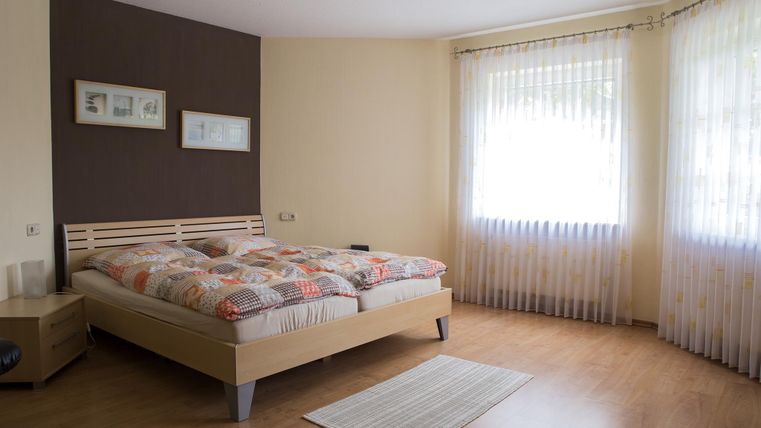 A bright bedroom with a double bed and colorful bedcovers. Large windows provide plenty of daylight and a cozy atmosphere.