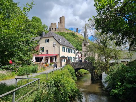 A picturesque view of the city with a historic building and a bridge over the river. In the background, a castle rises on a hill under a cloudy sky.