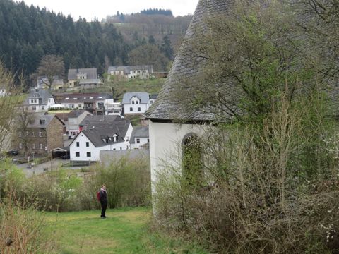 Eine kleine Stadt mit weißen Häusern und einem historischen Gebäude im Vordergrund. Im Hintergrund sind bewaldete Hügel sichtbar.