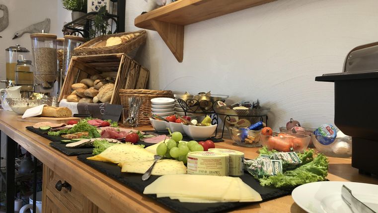 Ein reichhaltiges Frühstücksbuffet mit verschiedenen Käsesorten, Wurst, Obst und frischem Brot. Die Holzplatte bietet eine appetitliche Auswahl an Leckereien.