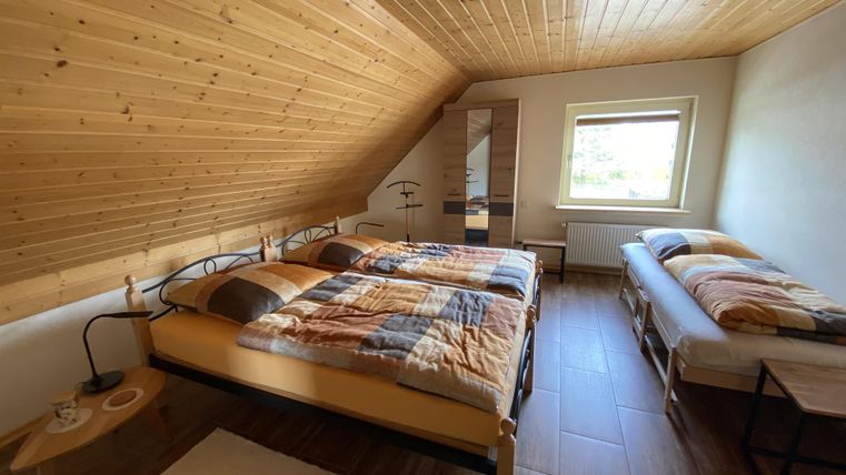Ein gemütliches Schlafzimmer mit zwei Doppelbetten und einem Einzelbett. Der Raum hat Holzboden und eine schlichte, einladende Einrichtung.