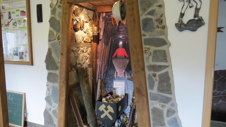 Eine dekorative Nische im Naturstein-Stil, die an einen Bergwerkschacht erinnert. Im Inneren sind Bergbauwerkzeuge und eine kleine Lore zu sehen.