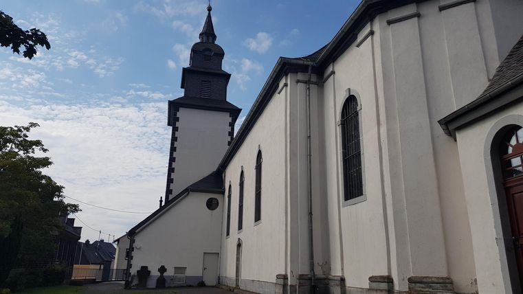 Eine alte Kirche mit einem hohen Turm und einer weißen Fassade. Der Himmel ist teilweise bewölkt.
