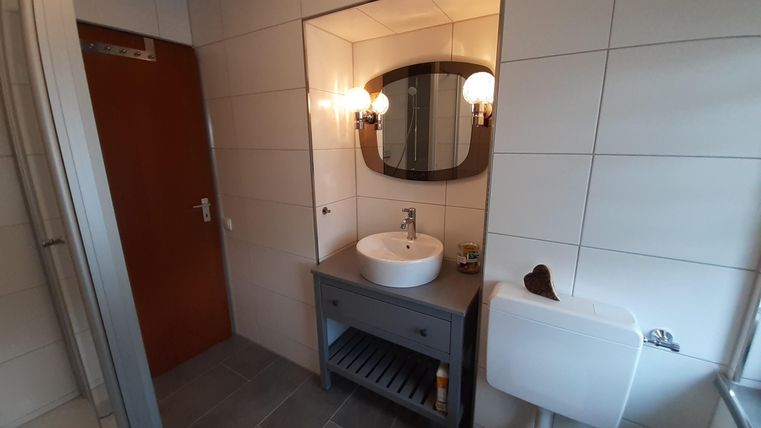 Ein modernes Badezimmer mit einem runden Spiegel und einer eleganten Waschtisch-Uni. Die Wände sind gefliest und der Boden hat graue Fliesen.