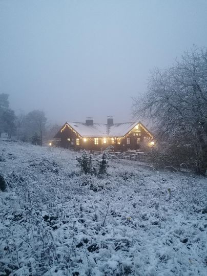 Ein schönes Holzhaus in einer verschneiten Landschaft. Die Lichter im Haus strahlen in der kalten, nebligen Umgebung.