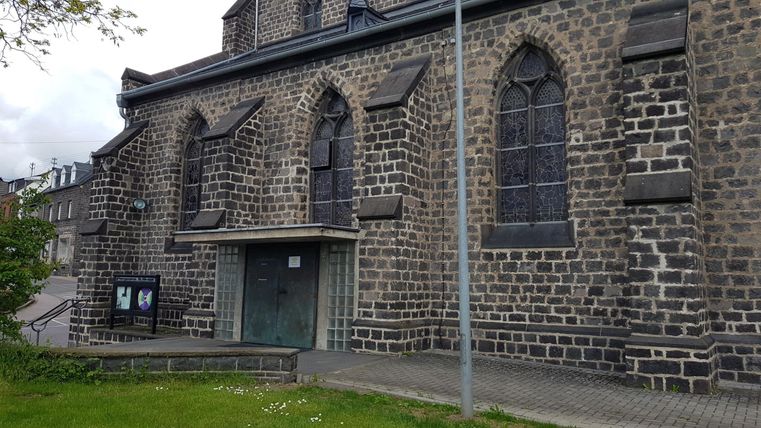Eine alte Steinkirche mit großen, gotischen Fenstern. Der Eingang ist modern und gut sichtbar.