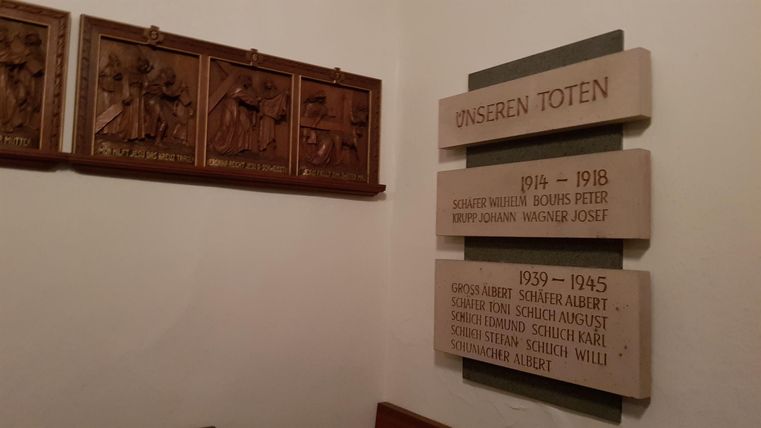 A wall with memorial plaques for the fallen from the years 1914 to 1945. Above them are ornate wooden reliefs.