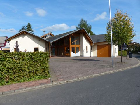 Ein modernes Haus an einer ruhigen Straße mit einem gepflegten Vorgarten. Der Himmel ist blau mit einigen Wolken.