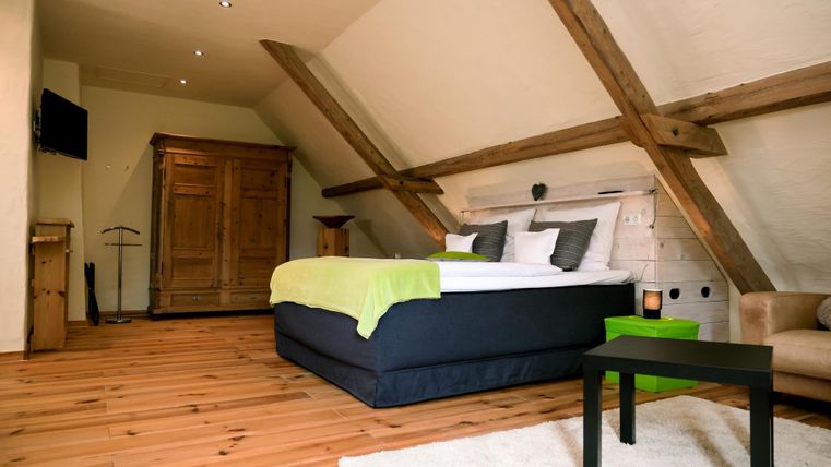 A cozy bedroom with a large bed and natural wooden floor. There is a beautiful headboard and elegant furniture in the room.