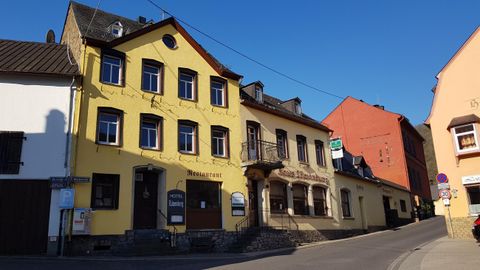 Ein gelbes Gebäude mit mehreren Fenstern an einer ruhigen Straße. Darüber strahlt ein klarer blauer Himmel.