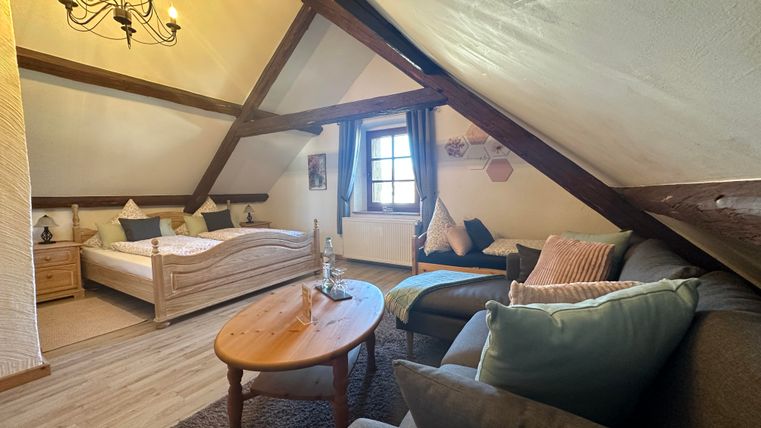 Ein gemütliches Schlafzimmer im Dachgeschoss mit einem Doppelbett und einem Wohnzimmerbereich. Das Zimmer hat Holzdetails und große Fenster, die viel Licht hereinlassen.