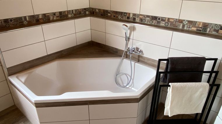 Eine moderne Eckbadewanne mit eleganter Armatur und Fliesen. Neben der Badewanne steht ein Handtuchhalter.