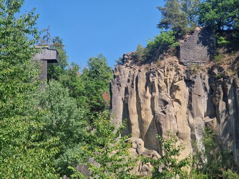 Eine beeindruckende Felslandschaft mit steilen Klippen und üppigem Grün. Im Hintergrund ist ein Aussichtsturm zu sehen.