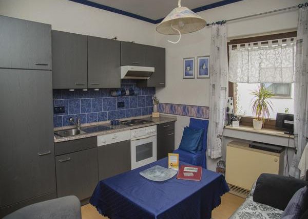 Eine moderne Küche mit dunklen Schränken und blauen Fliesen. Ein Tisch mit blauer Tischdecke und einige Küchenutensilien sind ebenfalls sichtbar.