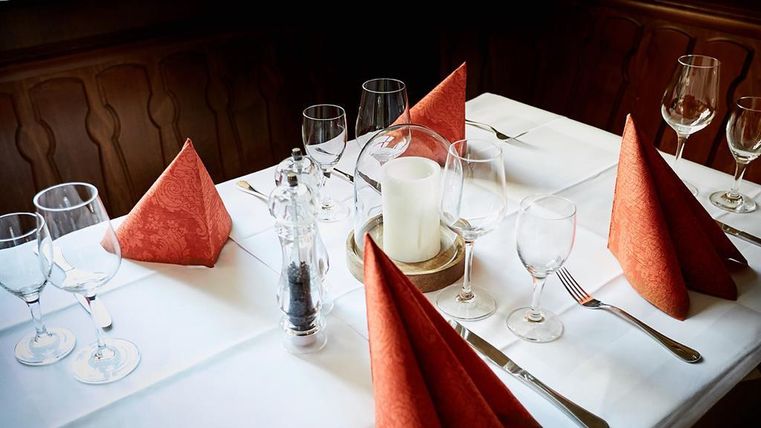 Ein elegant gedeckter Tisch mit roten Servietten und Weingläsern. Kerze und Besteck vervollständigen die stilvolle Atmosphäre.