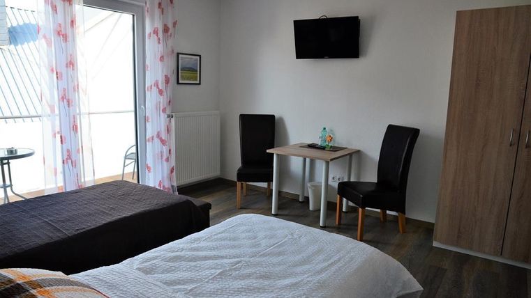 A cozy bedroom with two beds, a table and chairs. There is a window with access to the balcony and a TV on the wall.