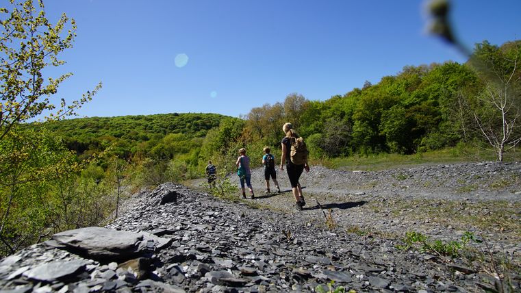 Gruppe von Wanderern auf einem Schieferweg in einer grünen Landschaft unter blauem Himmel.