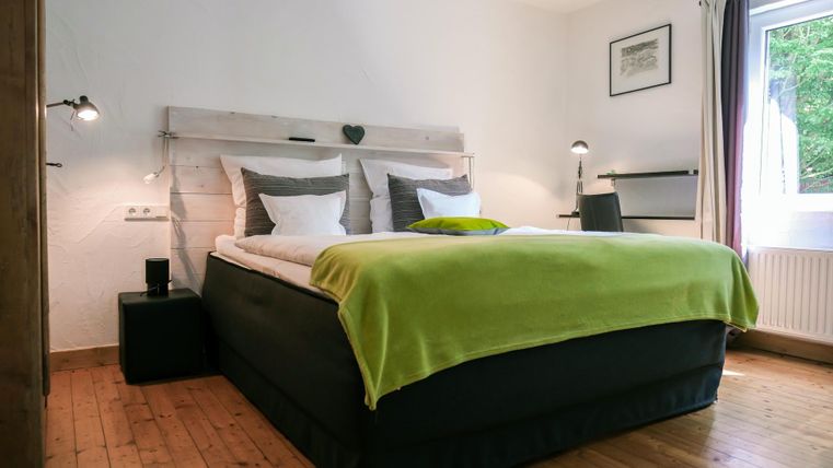 A cozy bedroom with a large bed and fresh white bedding. The walls are light and there is a window with a view outside.