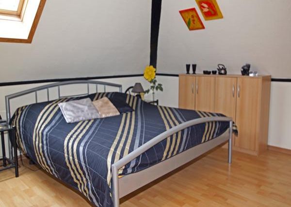 Ein gemütliches Schlafzimmer mit einem Bett und einem Holzschrank. Die Wände sind hell, und es gibt Dekorationen in warmen Farben.