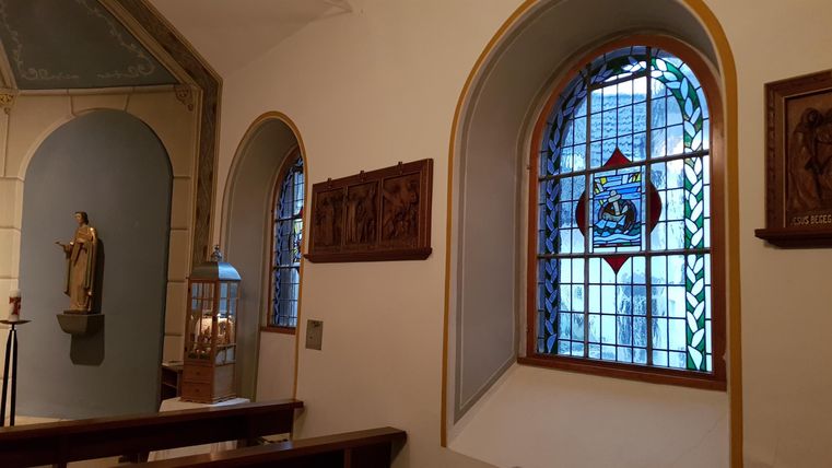 A beautiful interior with a colorful stained glass window and a statue. The walls are bright and simply designed.
