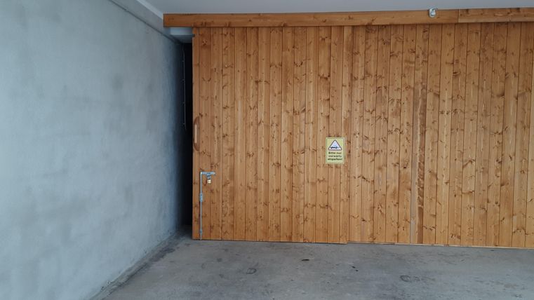 A wooden garage door with a warning sign. The room is empty and has a gray wall.