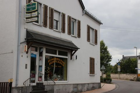 A small shop with a sign. The building is light gray and located at a street corner.