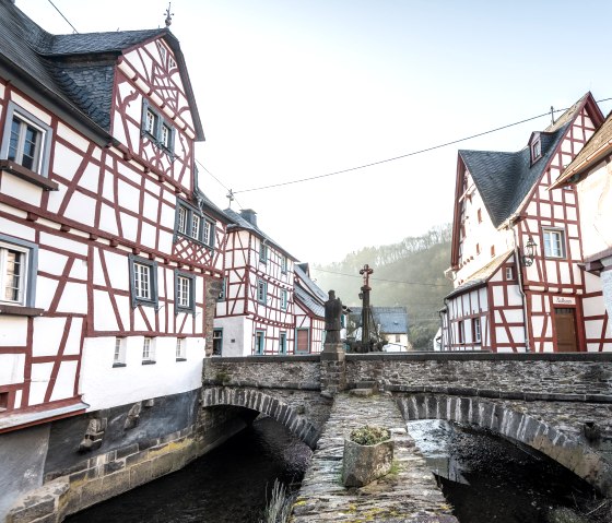 Fachwerkh&auml;user in Monreal mit einer steinernen Br&uuml;cke &uuml;ber einen kleinen Fluss. Eine Statue steht auf der Br&uuml;cke., &copy; Eifel Tourismus GmbH, D. Ketz