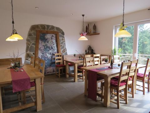 A cozy dining area with wooden tables and chairs. Large windows provide plenty of daylight and a view of the greenery.