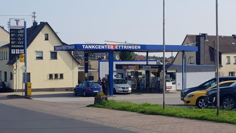 Eine Tankstelle mit mehreren Autos und einem klaren Himmel. Im Hintergrund sind Gebäude und Straßen zu sehen.