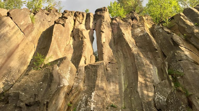 Eine beeindruckende Felsenwand mit glatten, hohen Steinen und kleineren Pflanzen. Der Himmel ist teilweise bewölkt, was die Szenerie dramatisch wirken lässt.