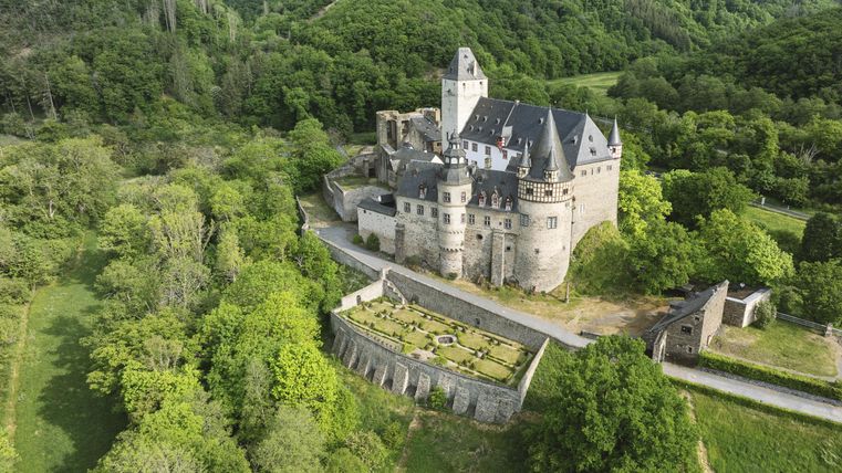 Eine beeindruckende Burg mit Türmen und einem Garten umgeben von Wald.