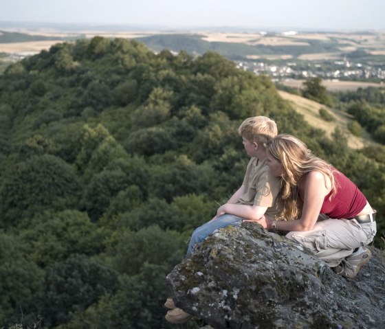 Zwei Personen sitzen auf einem Felsen und blicken auf die bewaldete Landschaft des Ettringer Bellbergs., &copy; Traumpfade/Kappest