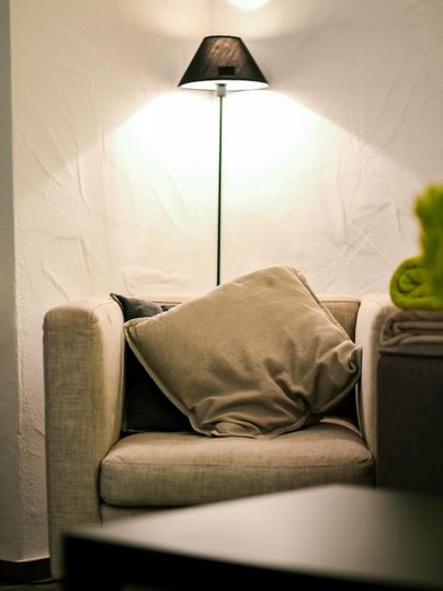 A cozy armchair with a cushion, underneath is a floor lamp. The wall is bright and textured, creating an inviting atmosphere.