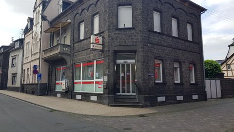A gray building on a street corner with large windows. In front of the building is a small sidewalk and street signs.