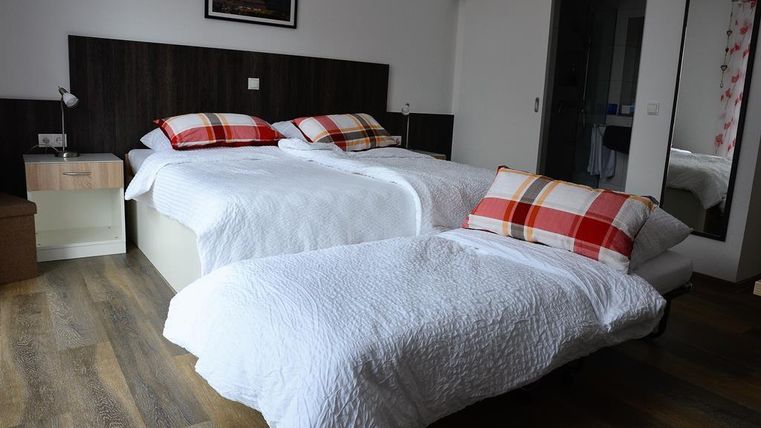 A cozy bedroom with two single beds and checked pillows. The room features stylish furniture and plenty of natural light.