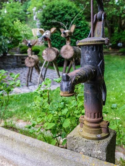 An old hand pump stands in the foreground. In the background, there are intricate metal sculptures of animals.