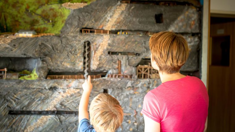 Eine Mutter und ihr Kind betrachten ein detailliertes Diorama mit Bergbauszene. Der Junge zeigt auf einen besonderen Bereich der Darstellung.