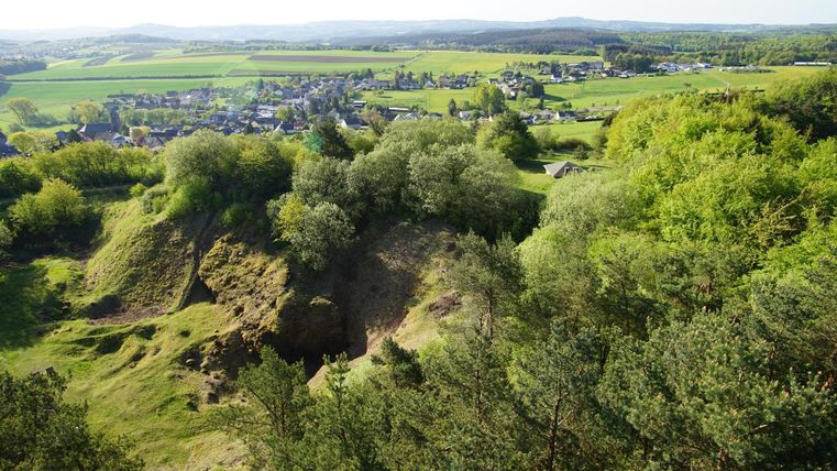 Eine malerische Landschaft mit sanften Hügeln und üppigem Grün. Im Hintergrund ist eine kleine Stadt und der weite Himmel sichtbar.