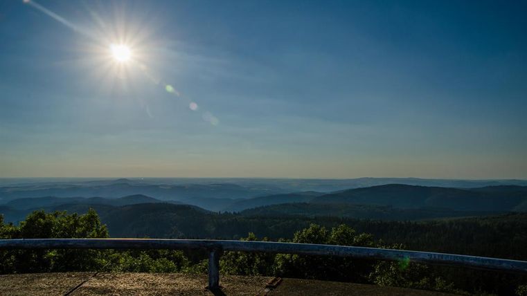 Ein Blick auf eine malerische Gebirgslandschaft mit sanften Hügeln und einem klaren Himmel. Die Sonne strahlt hell über der Aussicht.