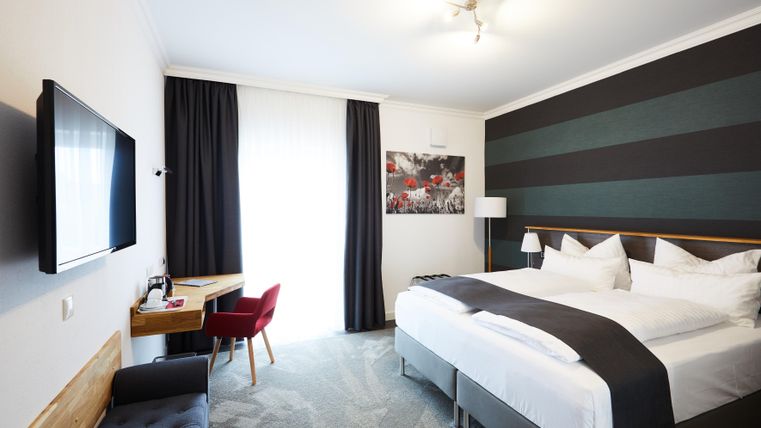 A modern hotel room with a large bed and a workspace.
Bright colors and large windows create a pleasant atmosphere.