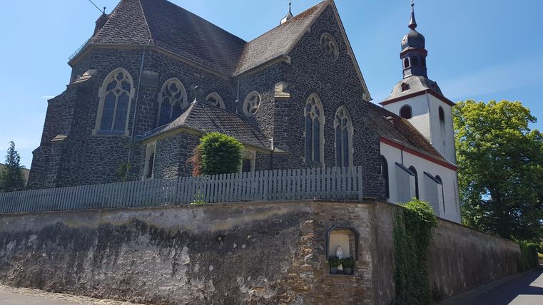 Eine alte Kirche mit beeindruckender Architektur steht auf einem Hügel. Neben der Kirche befindet sich ein kleiner Baumbereich und ein klarer blauer Himmel.