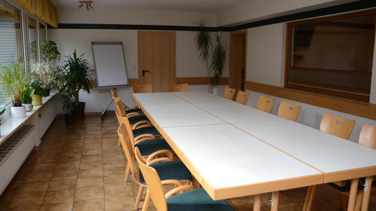 Ein Konferenzraum mit einem langen Tisch und Stühlen. Pflanzen und ein Flipchart sind im Raum vorhanden.