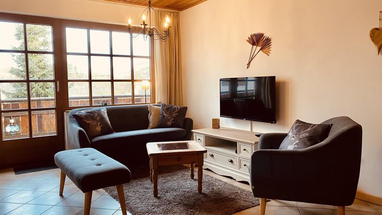 Ein gemütliches Wohnzimmer mit zwei Sofas und einem Couchtisch. Großes Fenster mit Blick nach draußen und ein Fernseher an der Wand.