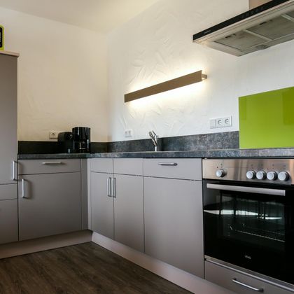 A modern kitchen with gray cabinets and a green backsplash. The equipment includes a stove, a refrigerator, and a microwave.
