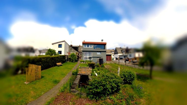 Ein modernes Haus in einem ruhigen Wohngebiet, umgeben von einem grünen Garten. Der Himmel ist teilweise bewölkt.