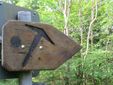 Holzwegweiser mit Pfeil und Punkt im Wald.