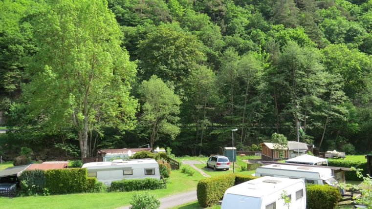 Ein malerischer Campingplatz inmitten von grünen Bäumen. Wohnmobile und Stellplätze sind in einer ruhigen Umgebung angeordnet.