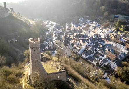 Luftaufnahme von Monreal mit einer Burg im Vordergrund und Fachwerkh&auml;usern im Tal. Die Landschaft ist von B&auml;umen und H&uuml;geln umgeben., &copy; Eifel Tourismus GmbH, D. Ketz