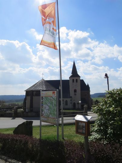 A church with a distinctive tower stands in the foreground. In the background, bright clouds and a blue sky are visible.