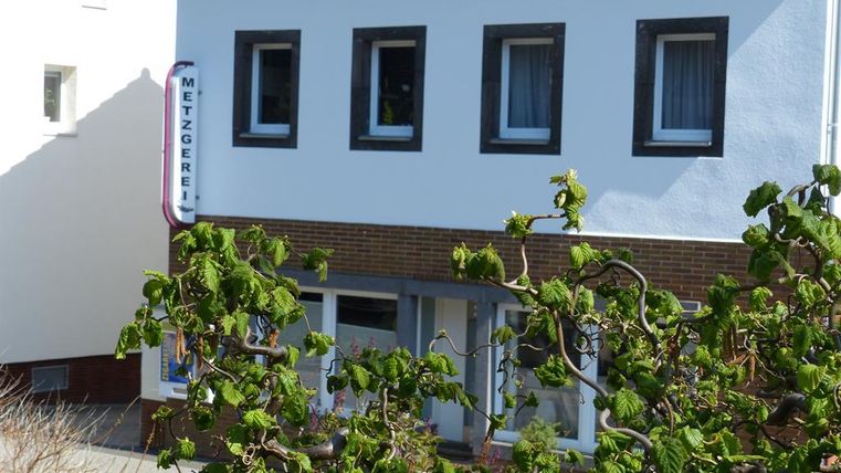 Ein Metzgerei-Geschäft in einem Wohngebiet. Die Fassade ist weiß mit großen Fenstern und einem Schilder mit dem Wort "Metzgerei".